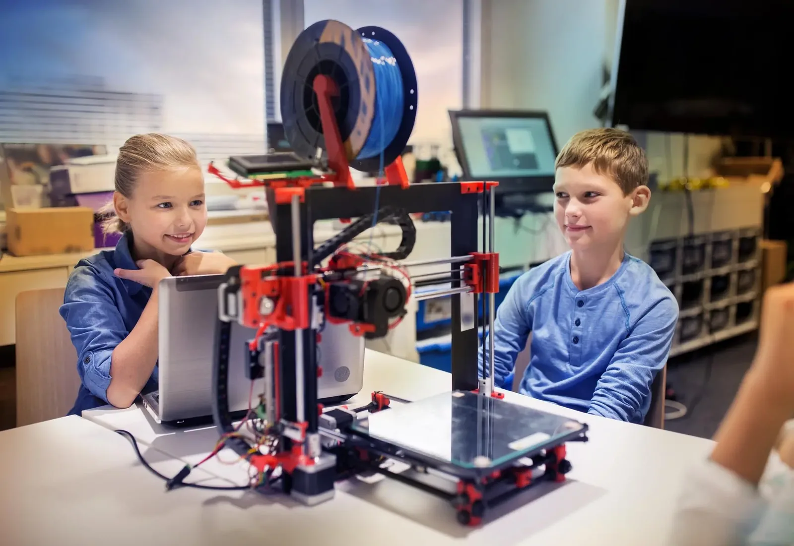 Dziewczynka i chłopiec obserwują pracującą drukarkę 3D