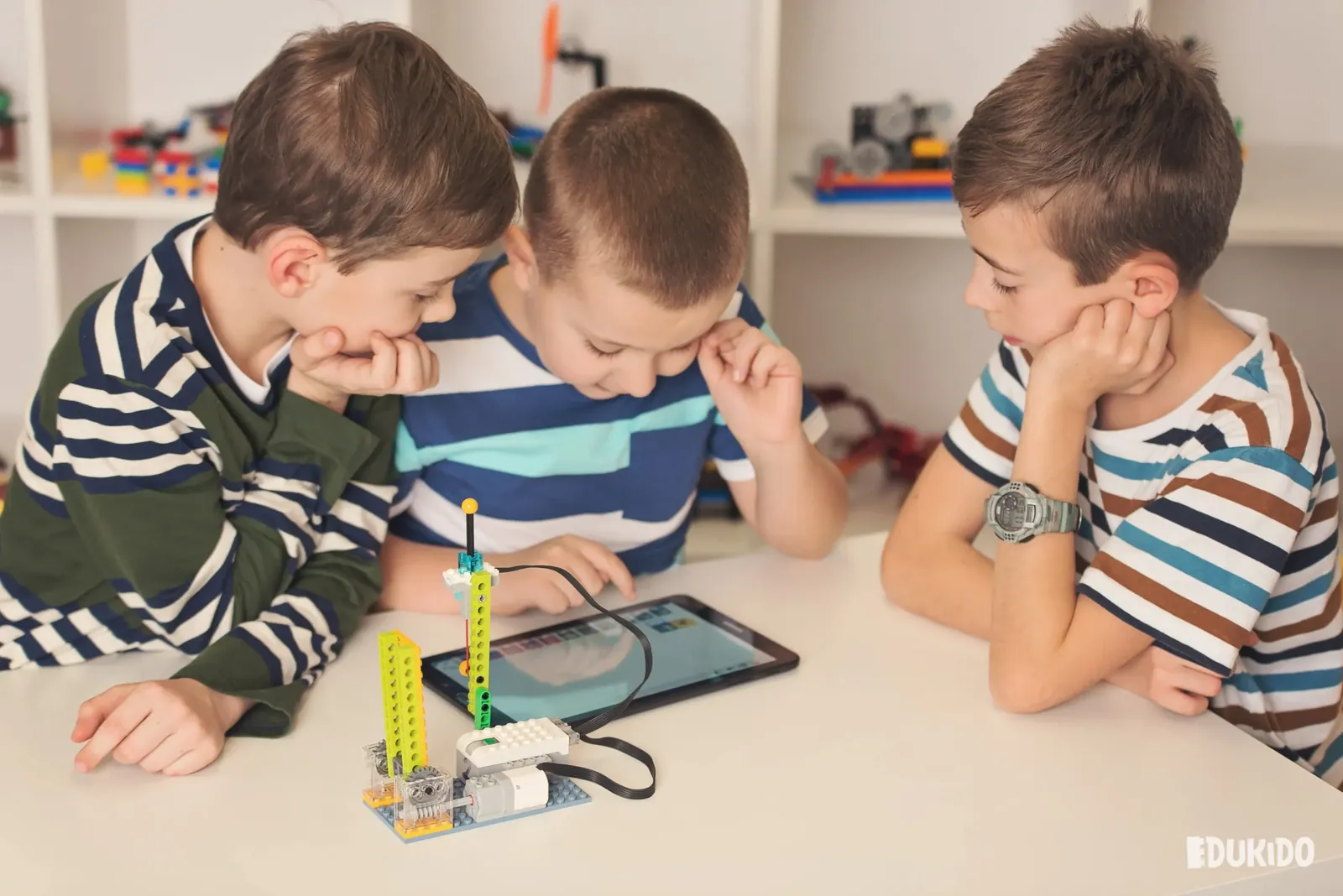 Trzej chłopcy przy stole obsługują model z klocków sterowany z tabletu